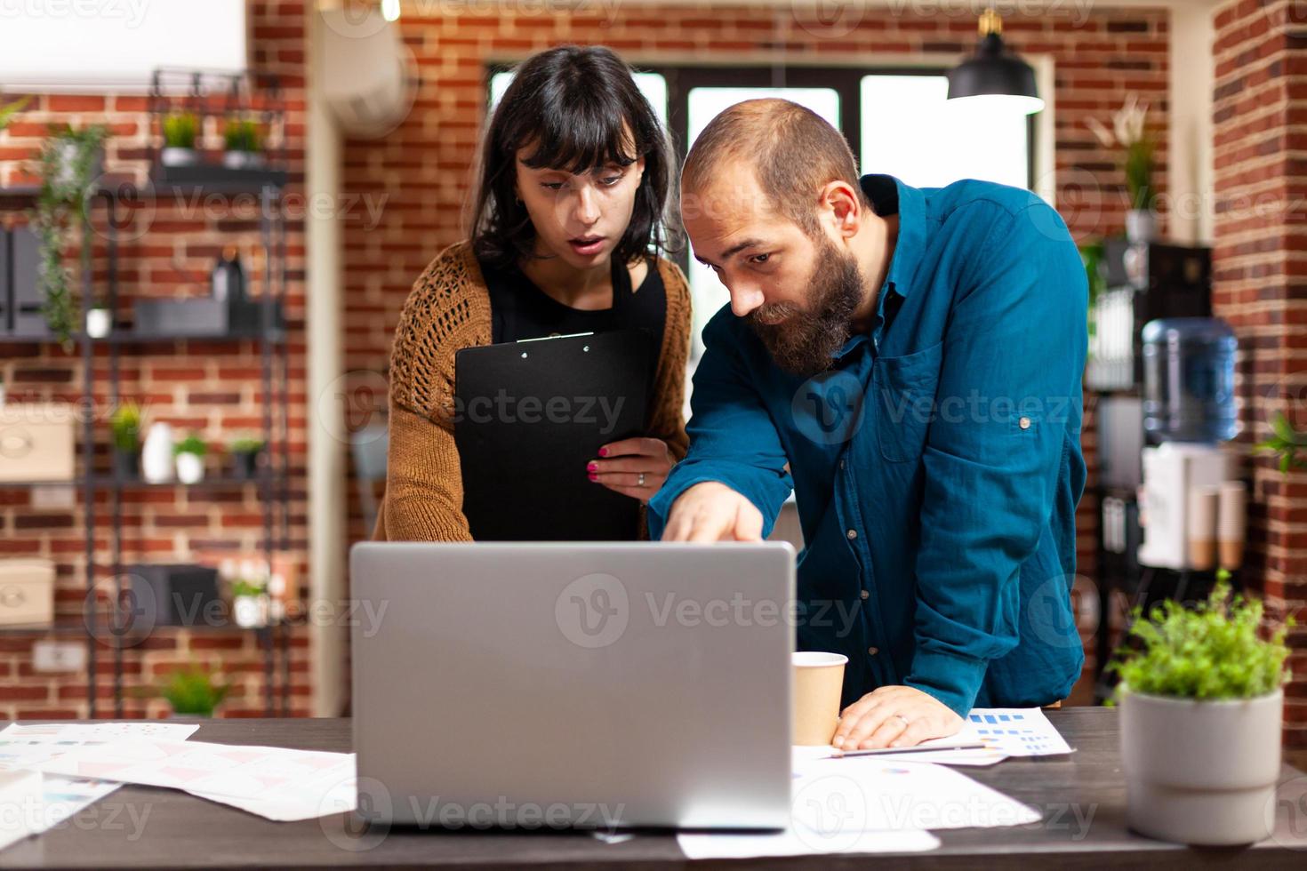 Communication team looking at management strategy using laptop analyzing business paperwork photo