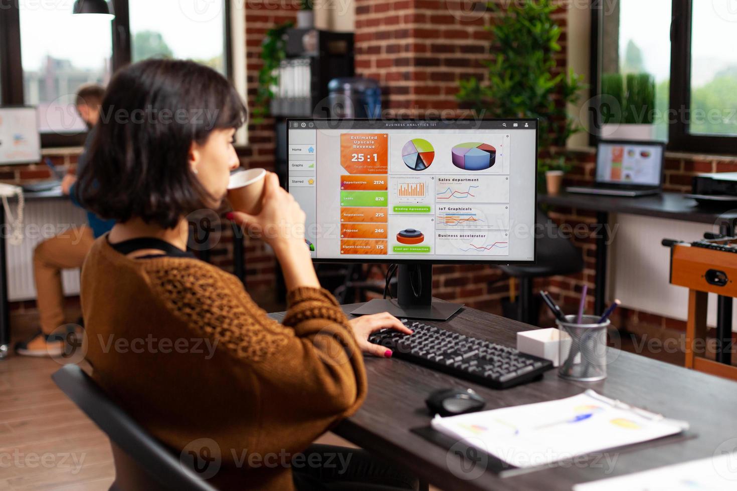 Businesswoman holding cup of coffee analyzing financial graphs typing marketing strategy photo