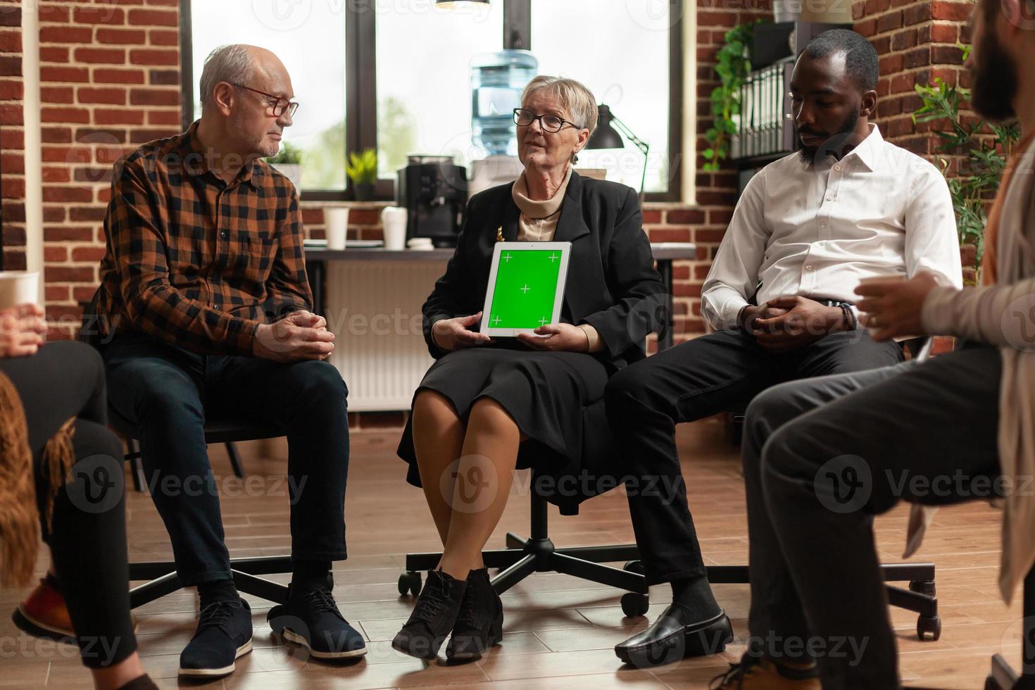 Psiquiatra en una reunión mostrando tableta con pantalla verde a un grupo de personas foto