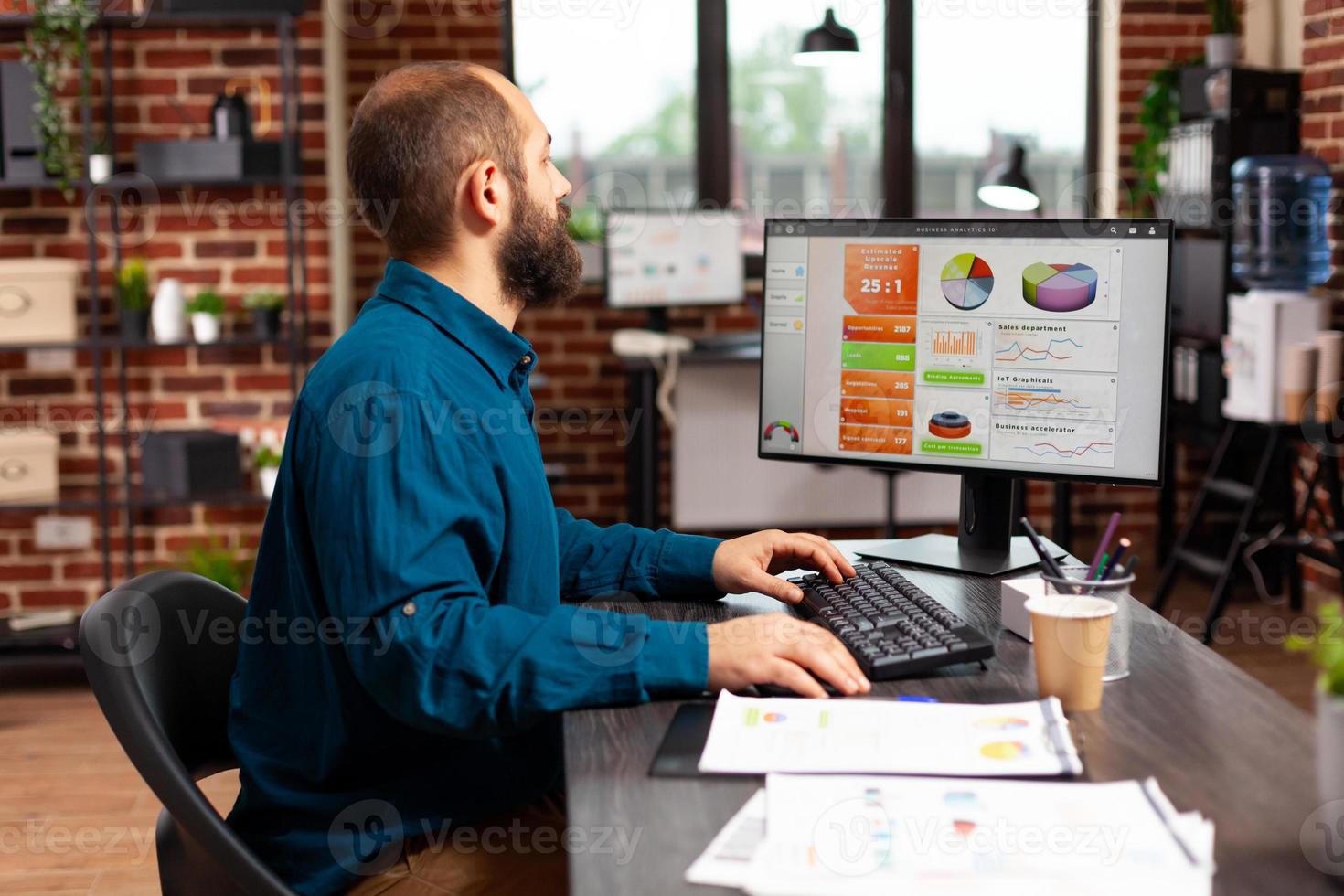 Businessman sitting at desk typing marketing strategy on computer keyboard photo