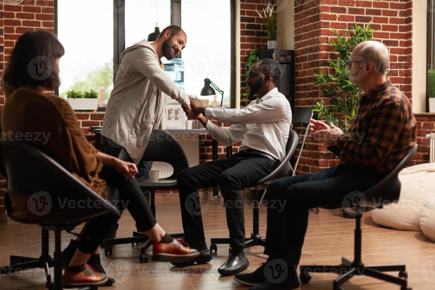 Multi ethnic people doing handshake to celebrate progress at aa group therapy photo