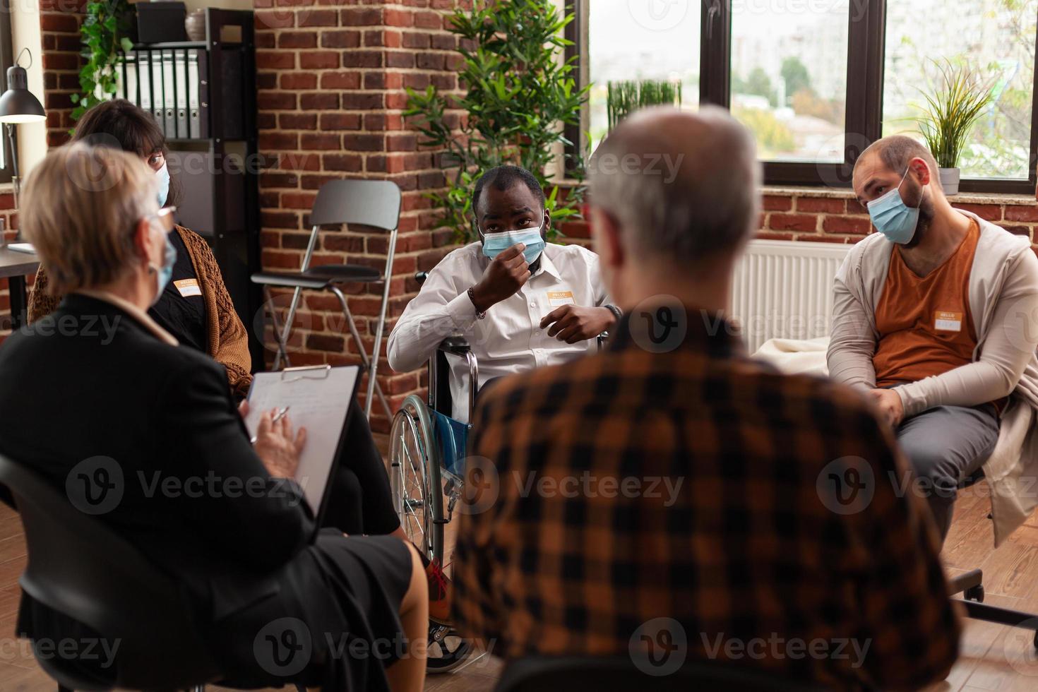 Hombre afroamericano sentado en silla de ruedas, asistiendo a una reunión con personas foto