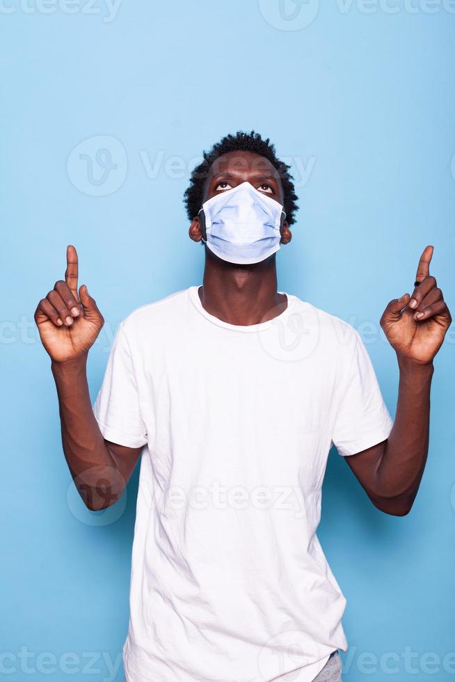Hombre casual con mascarilla contra el coronavirus apuntando con el dedo hacia arriba foto