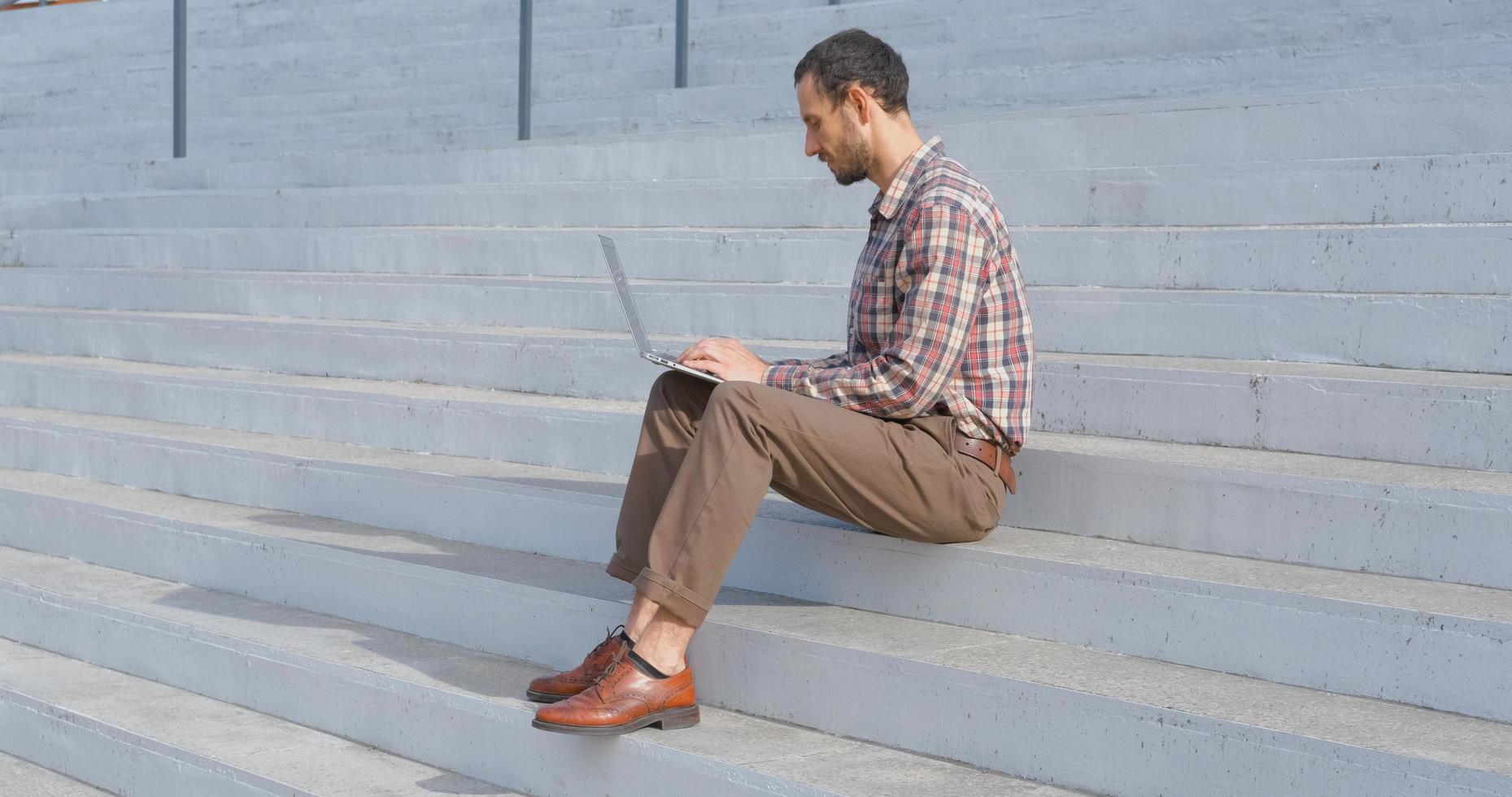 young male businessman sitting on the stairs outdoors working with laptop photo