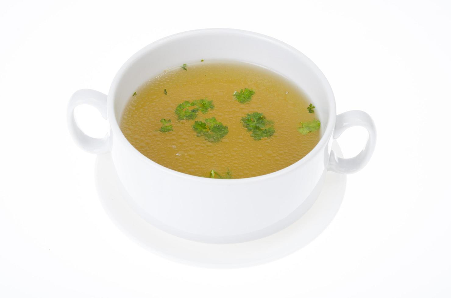 Transparent meat broth with herbs in white plate photo