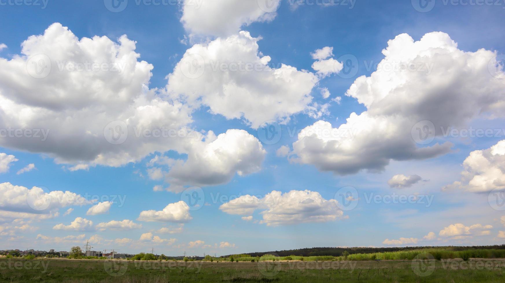 A field with a clear blue sky filled with white clouds in the background in bright sunny summer weather without wind or rain. photo