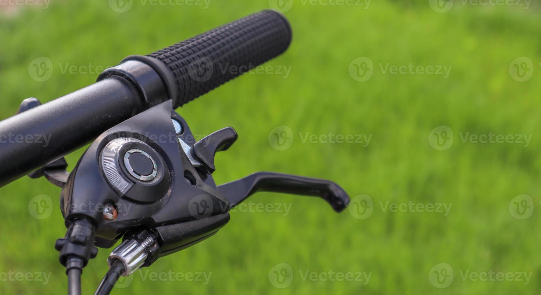 Mountain bike steering wheel on green grass background. Details of sporting events. Close up black mountain bike knob and derailleur knob, left shifter. photo