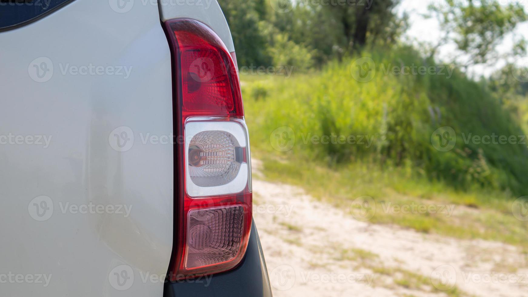 Right rear headlight. The rear of a small passenger hatchback or SUV of a white car with a group of taillights and a part of the trunk lid on the right. Red turn signal and brake light. photo