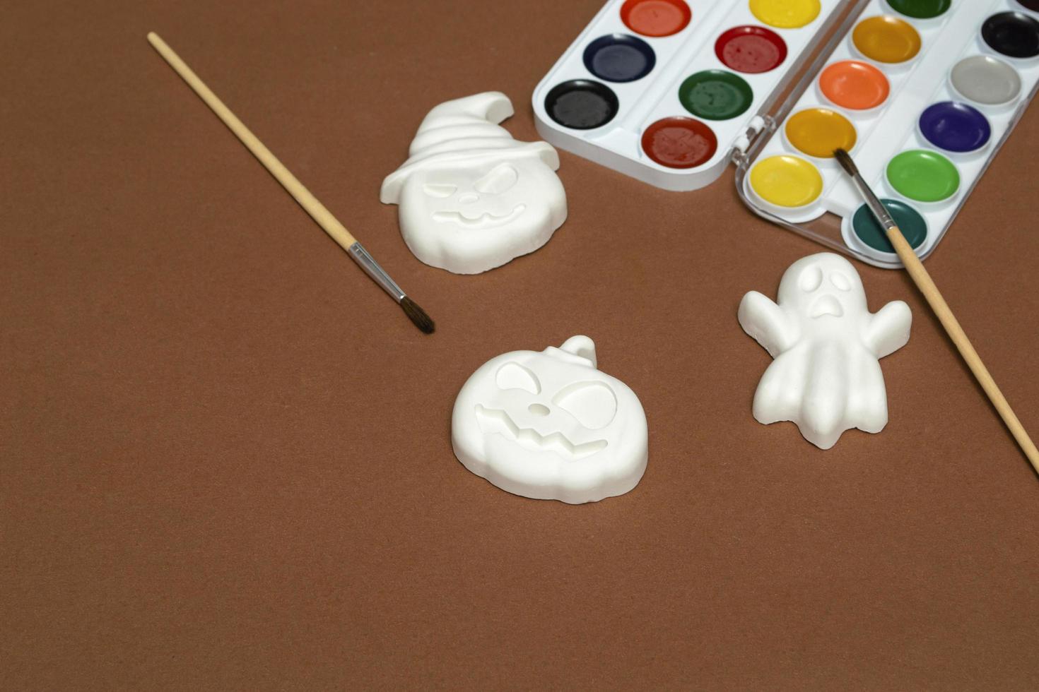 Halloween crafts. Gibs figurines of pumpkins and ghosts in bright paint with a brush on a brown background, ready for drawing close-up photo