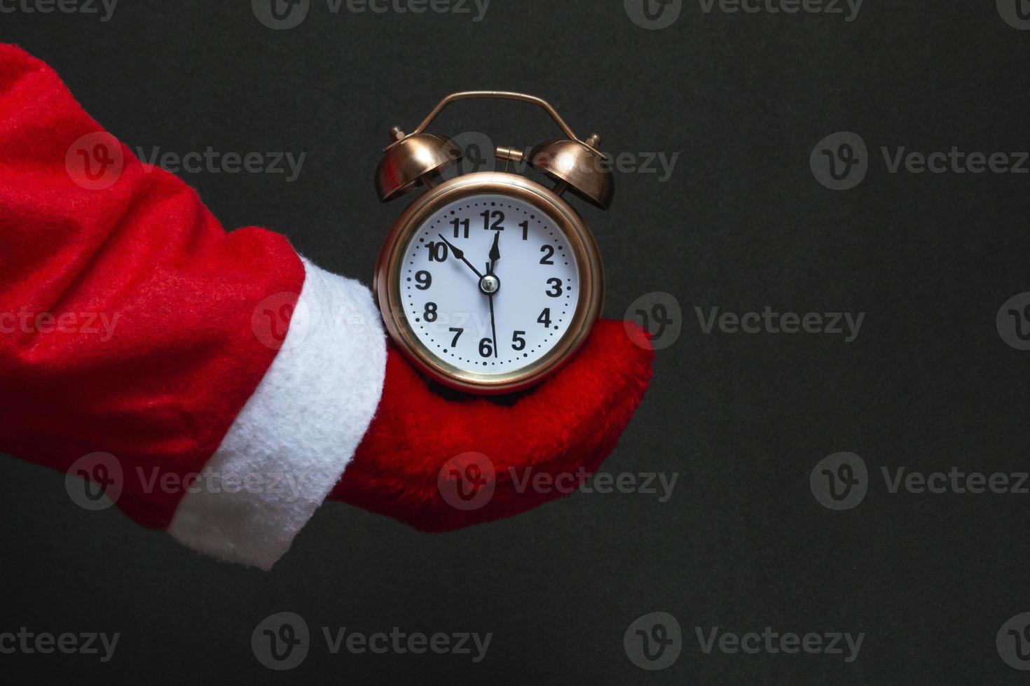 Festive concept. In the hand of santa claus an alarm clock of copper color on a black background. close-up photo