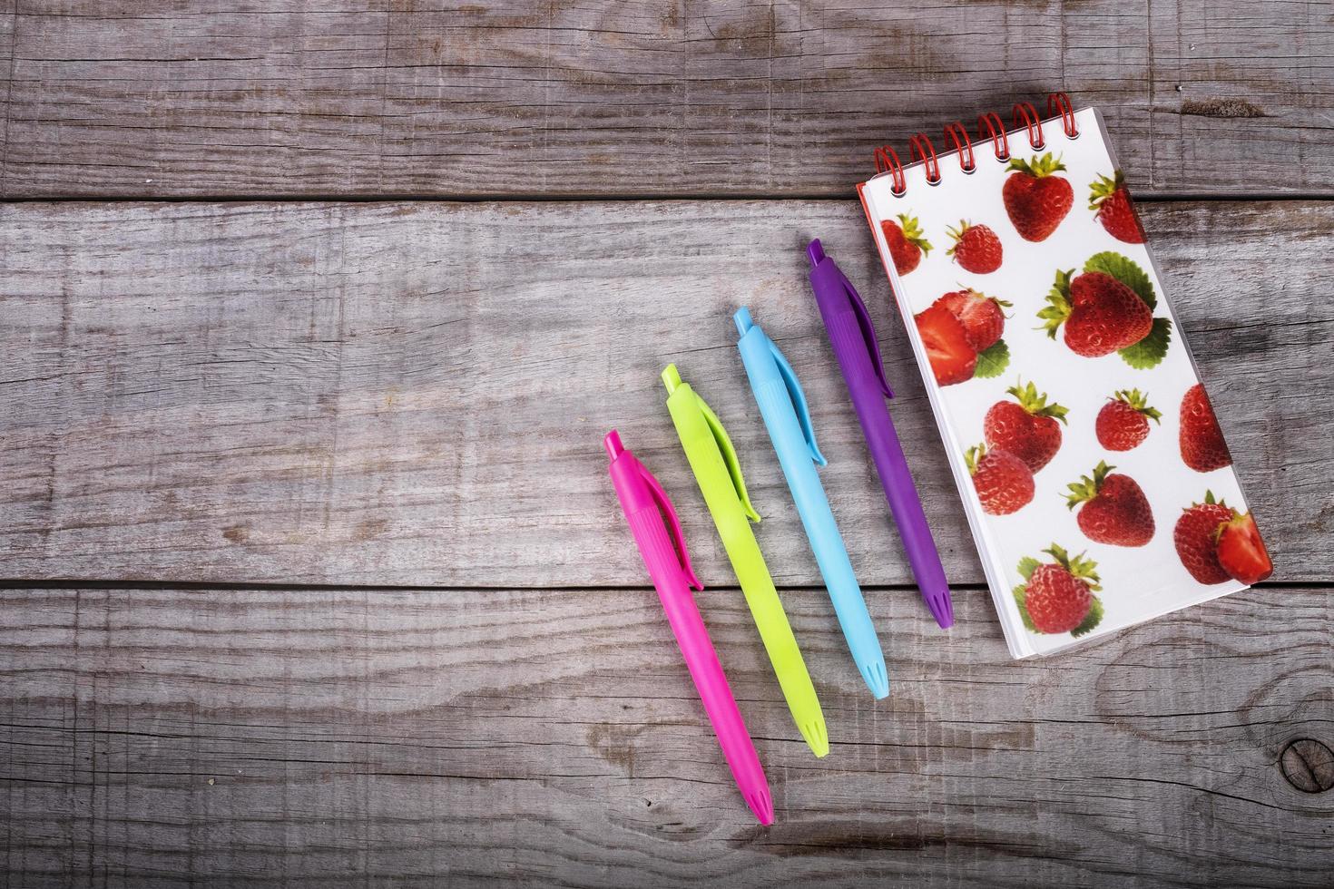 Cuaderno con fresas y juego de bolígrafos de colores sobre fondo de madera foto