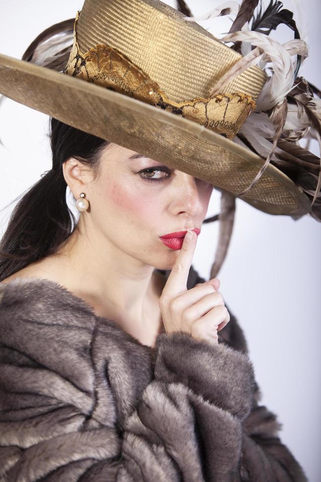 beautiful woman with hat and fur coat and finger in her mouth pointing silence photo