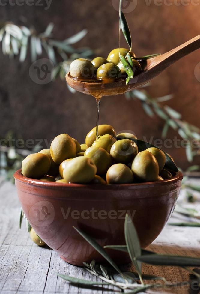 pouring oil on wooden spoon with olives over a filled bowl photo