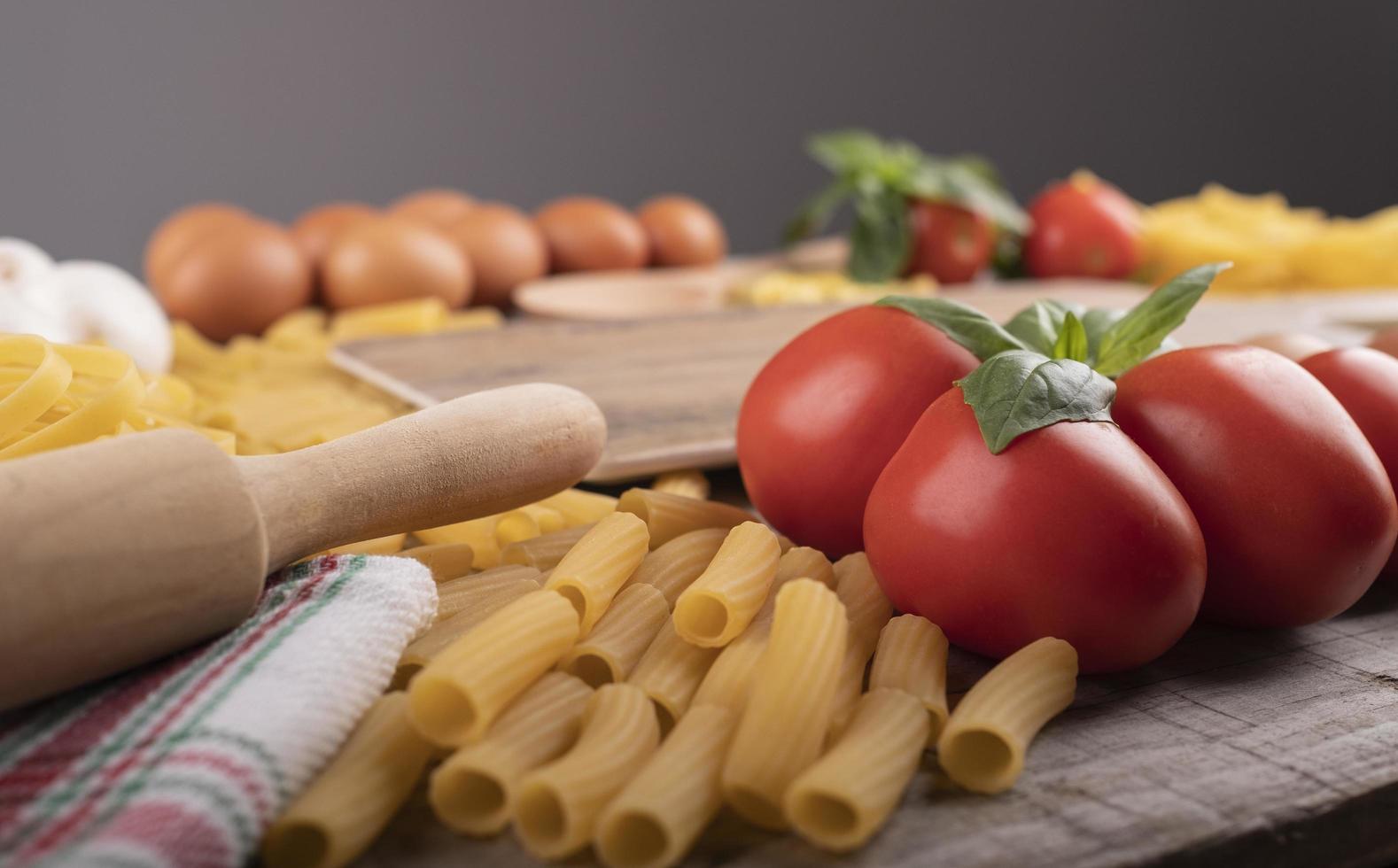 pasta, tomatoes and ingredients for italian restaurant with wooden kneader photo