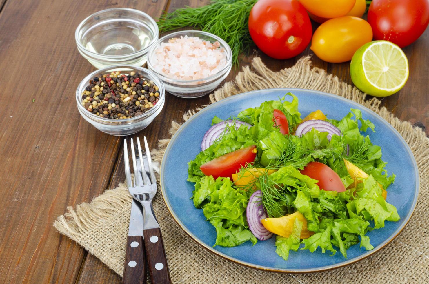 Light meal of green leaves of lettuce, yellow and red tomatoes, olive oil on wooden table. photo