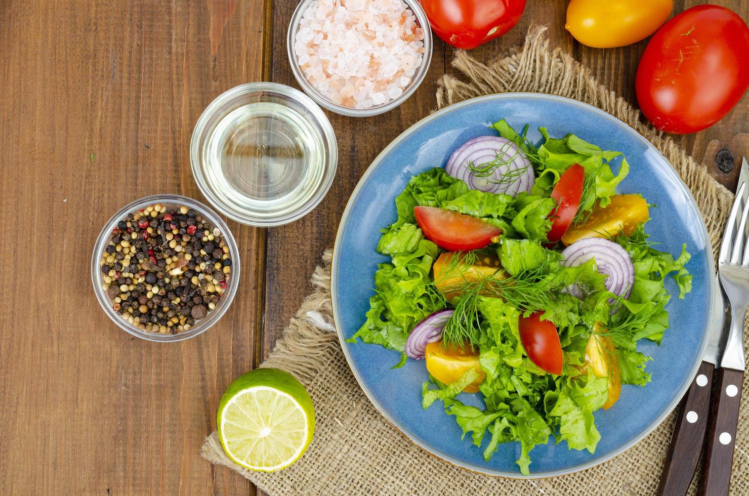 Light meal of green leaves of lettuce, yellow and red tomatoes, olive oil on wooden table. photo