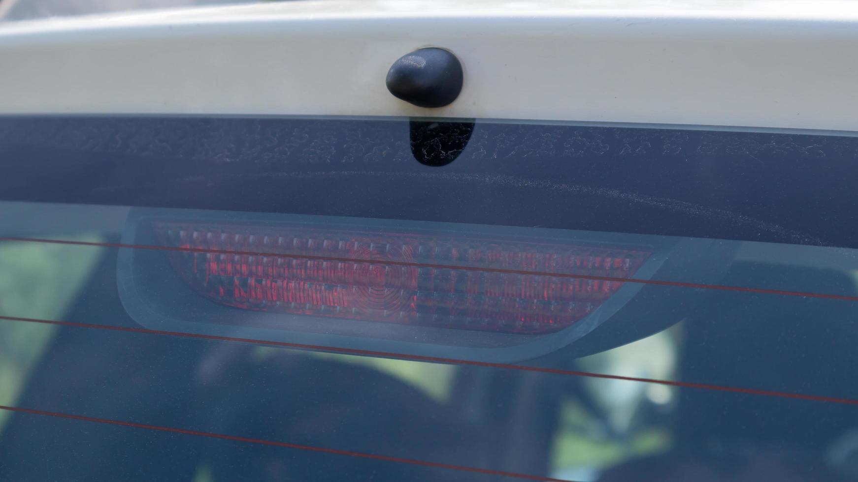 Rear window of a dusty white car with a stoplight behind glass, close-up. Red signals indicating vehicle braking. They turn on automatically when you press the brake and turn off when you release it. photo