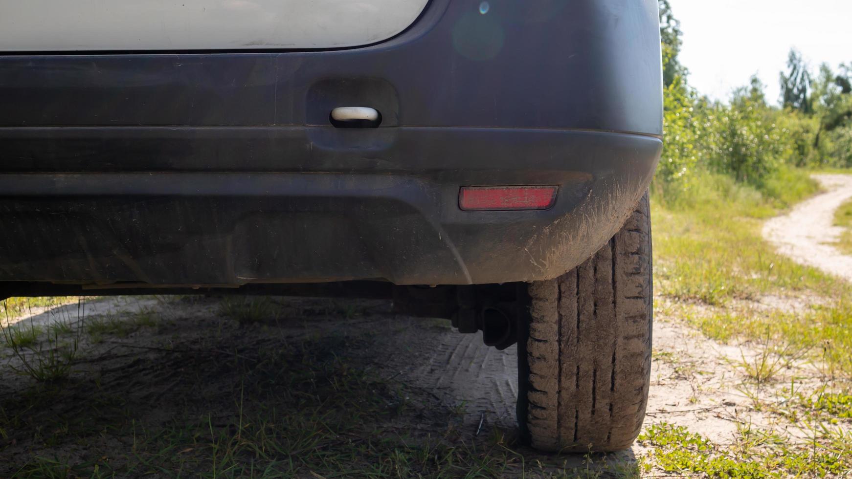 Passenger side of a white modern car on a dirt road, rear view of the bumper and wheel. Very low plan. photo