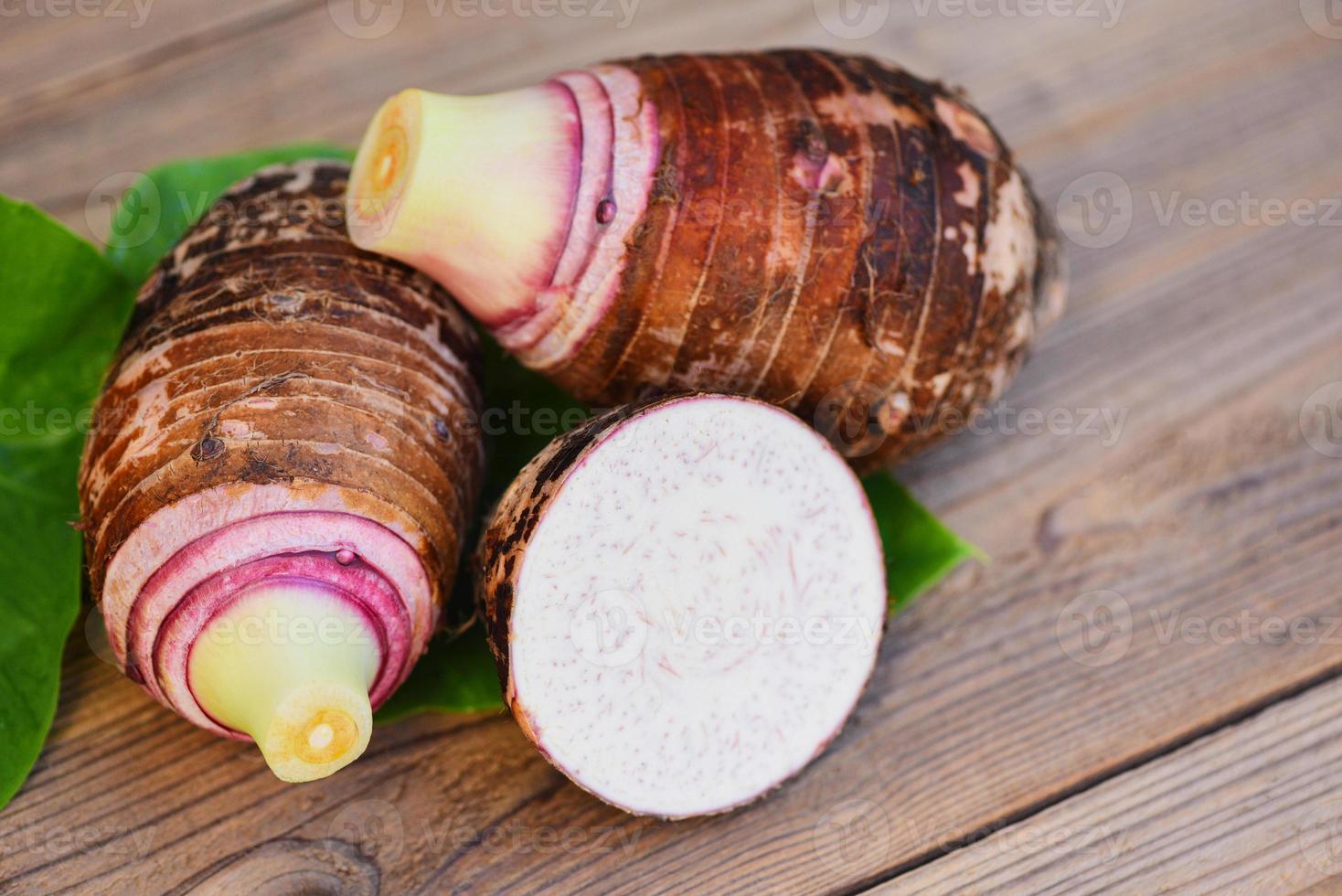 Taro root with half slice on taro leaf and wooden background, Fresh raw organic taro root ready to cook photo