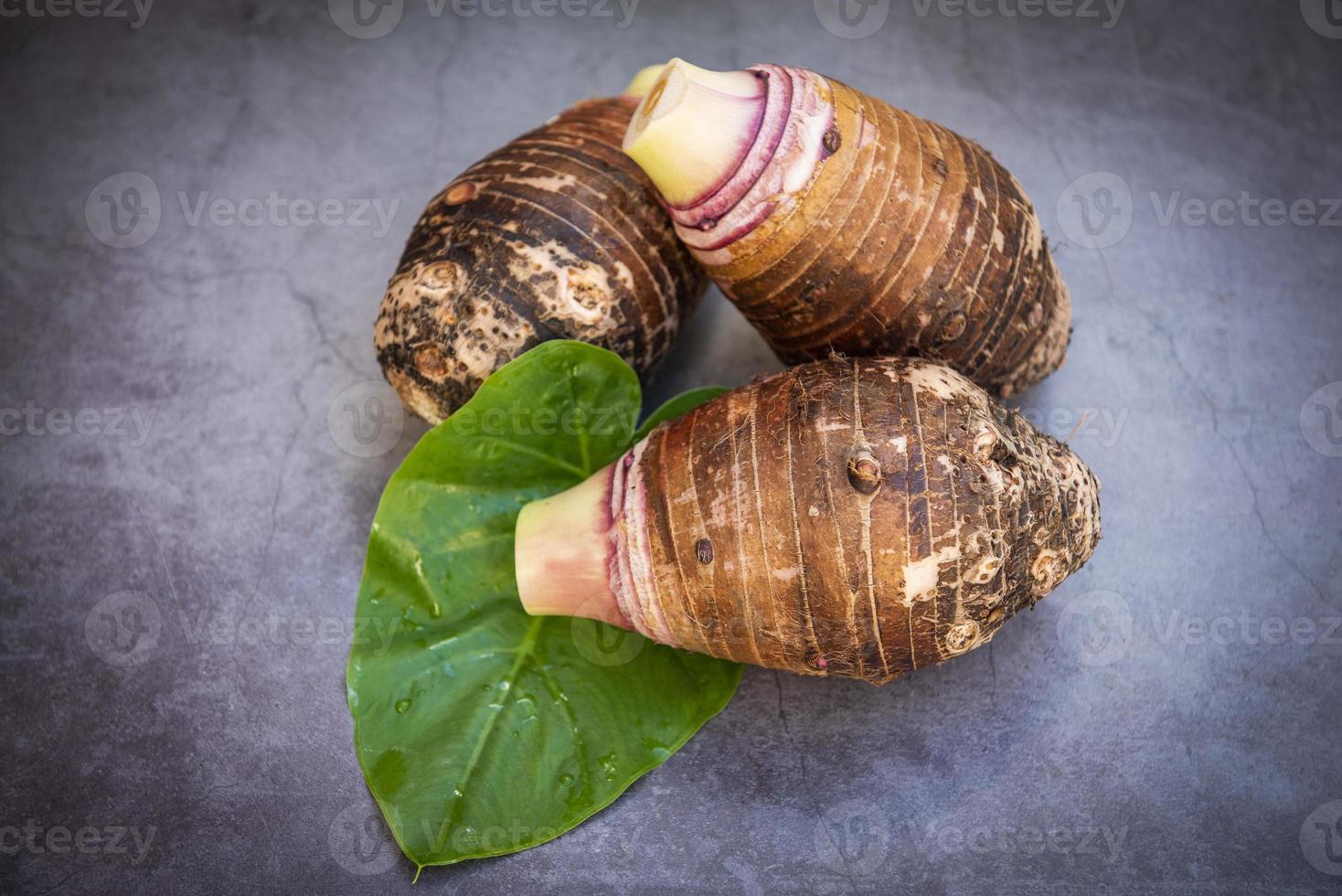 Taro root on taro leaf and dark background, Fresh raw organic taro root ready to cook photo
