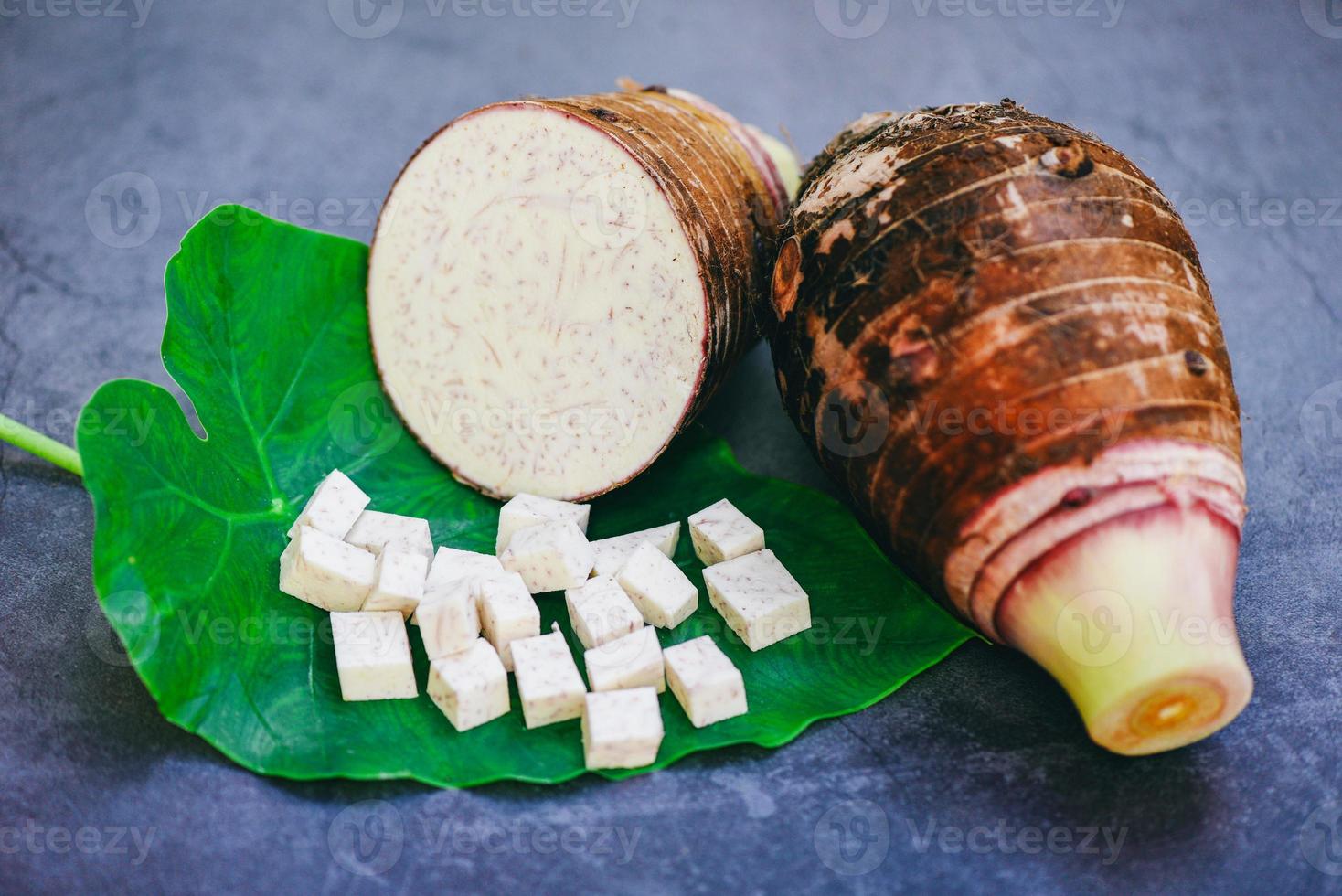 Taro root with half and slice cubes on taro leaf and wooden background, Fresh raw organic taro root ready to cook photo