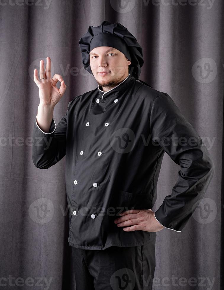 Male chef showing ok sign isolated on dark curtain background photo