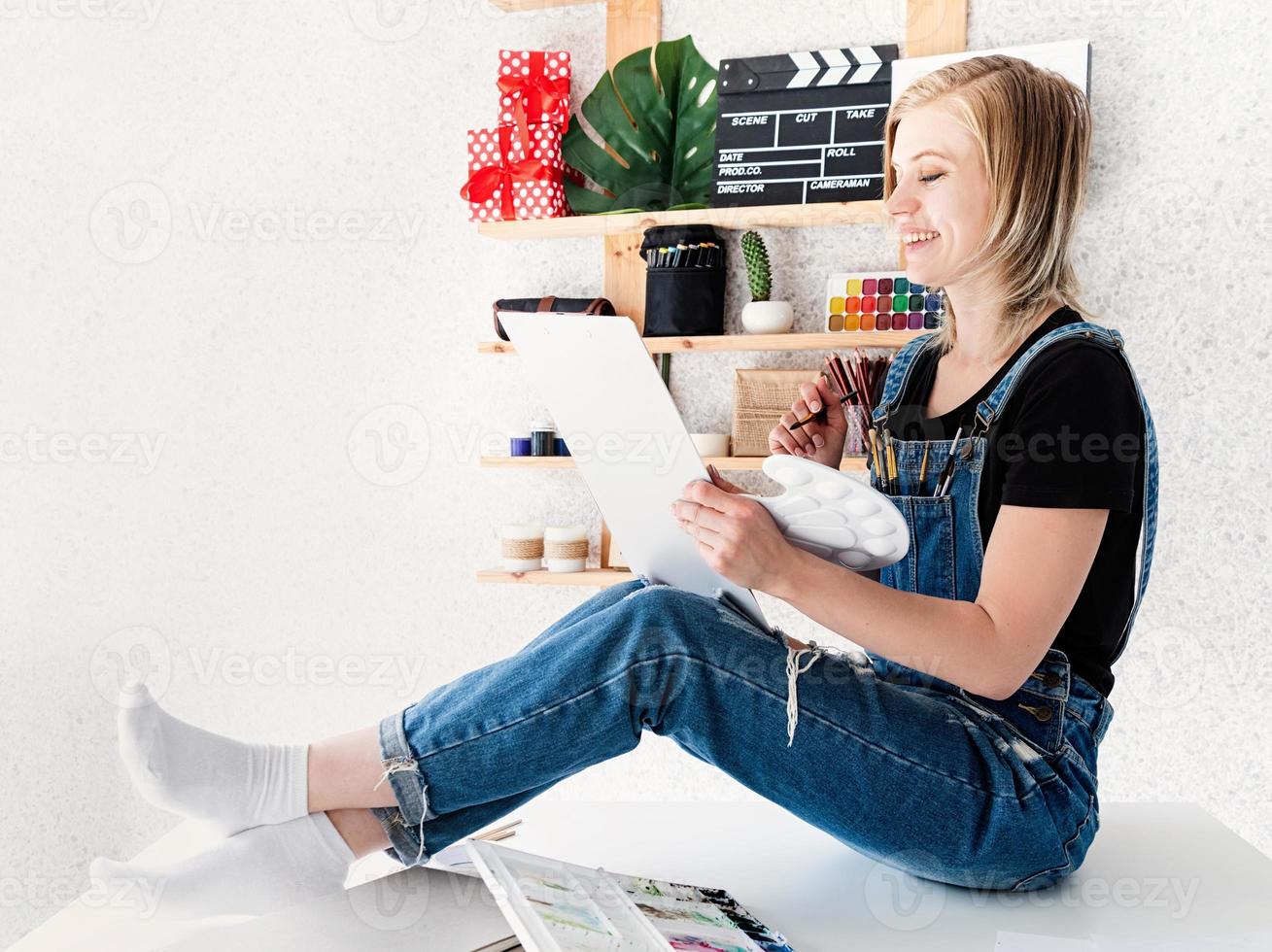 Riendo artista femenina dibujando en casa sentada en su escritorio foto