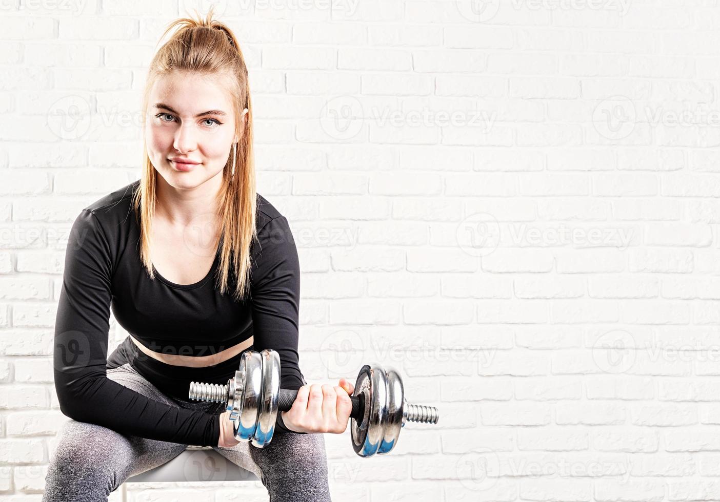 Deportiva joven sosteniendo una mancuerna entrenando sus bíceps foto