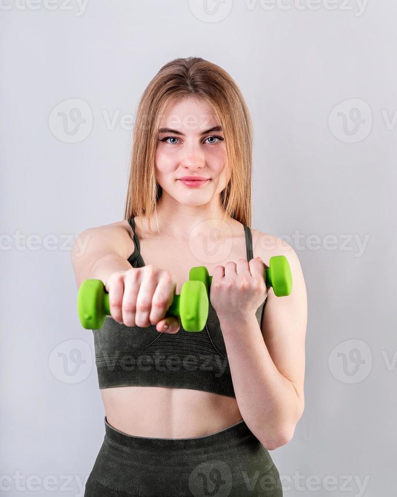 Joven deportiva haciendo ejercicios con pesas aislado en gris foto