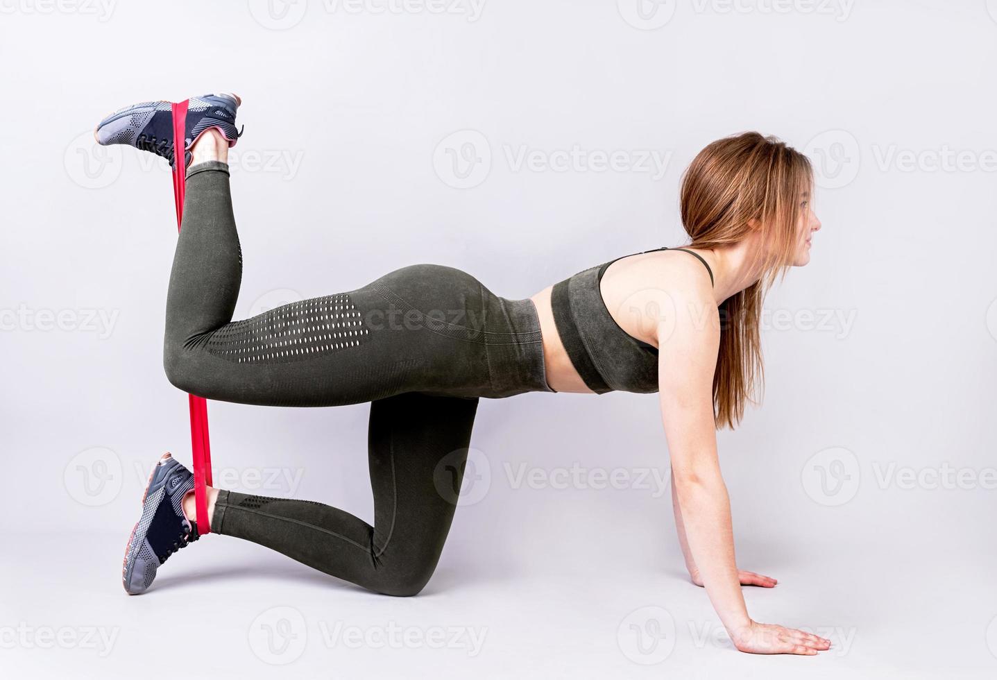 Young sportswoman doing the exercises on all fours arching back straightening leg up at home using rubber resistance band photo