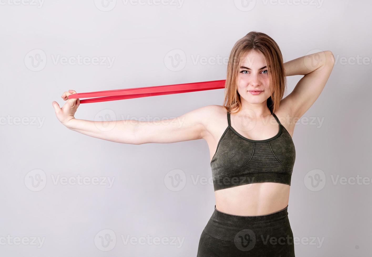 Young fit woman doing exercises with a resistance band isolated on gray photo