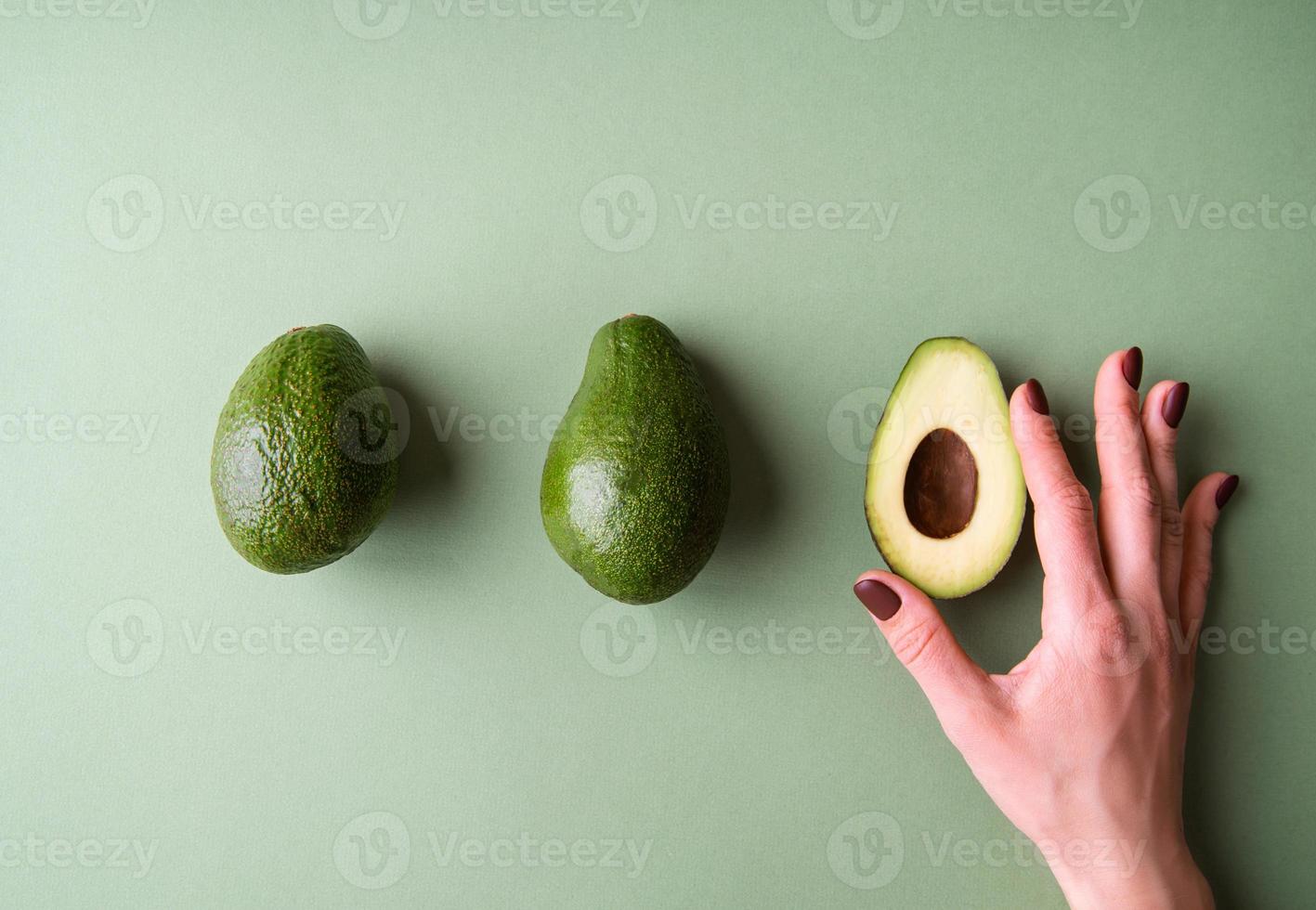 Woman hand holding a half of avocado on the green background top view photo