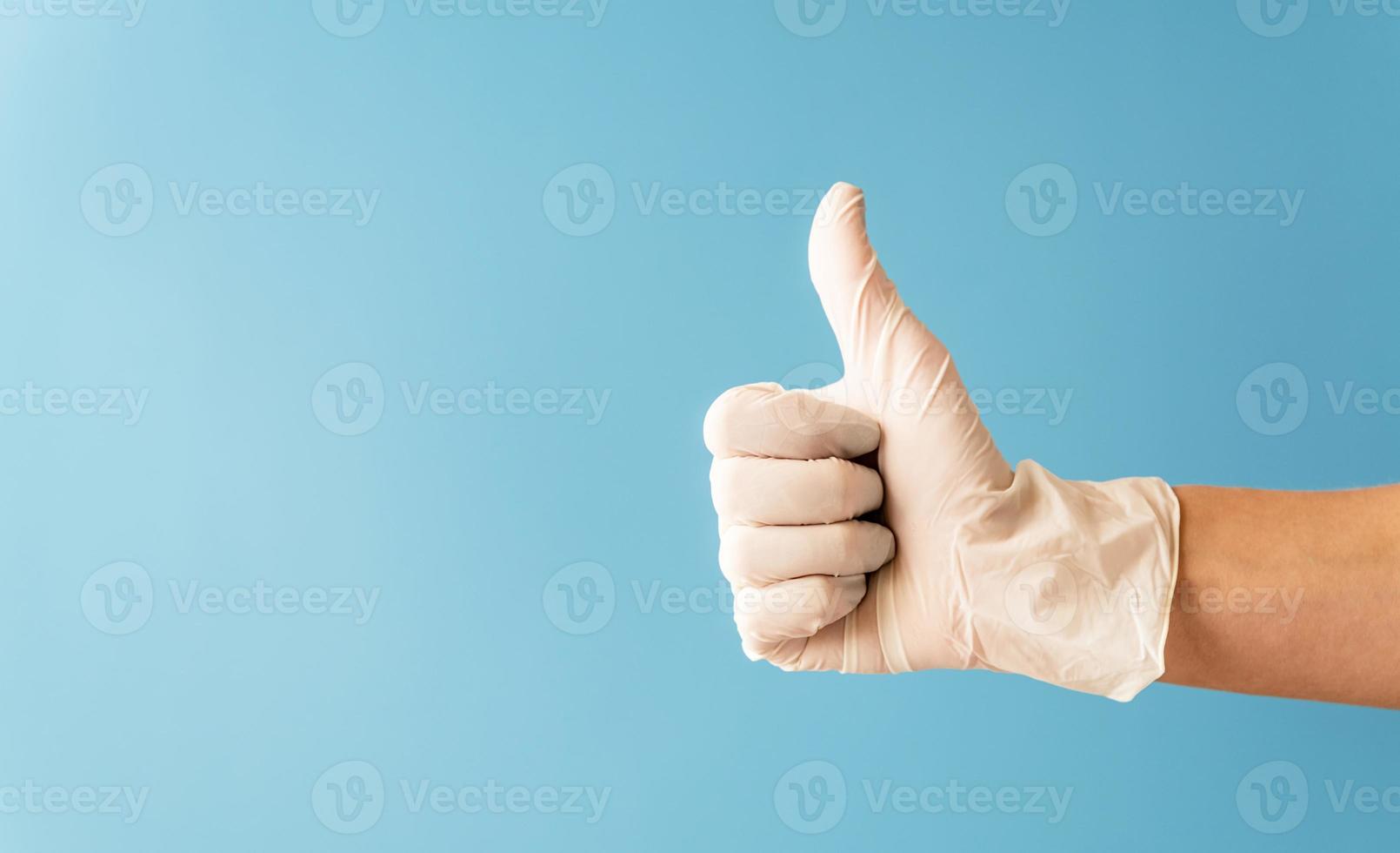 Hand wearing white rubber glove giving the thumbs up signal. photo