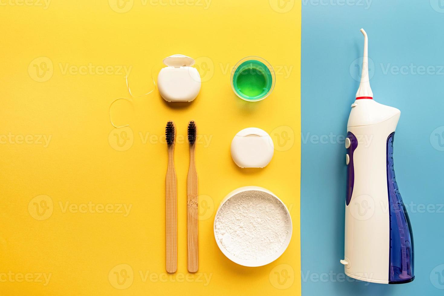 Dental tools, floss, mouth irrigator, toothbrushes, oral rinse and tooth powder top view on blue and yellow background photo