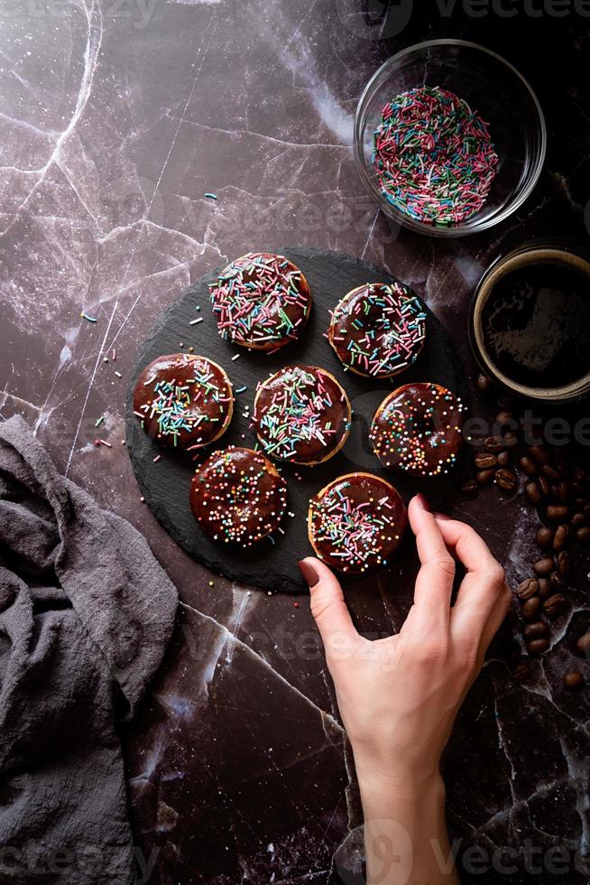 Donuts frescos con glaseado de chocolate y chispas de colores sobre fondo oscuro foto