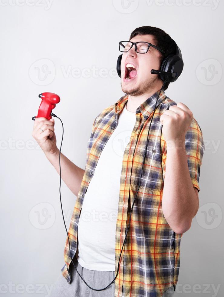 Gracioso joven gritando jugando videojuegos sosteniendo un joystick aislado sobre fondo gris foto