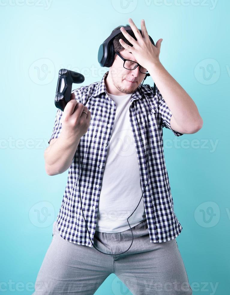 Joven decepcionado jugando videojuegos sosteniendo un joystick aislado sobre fondo azul. foto