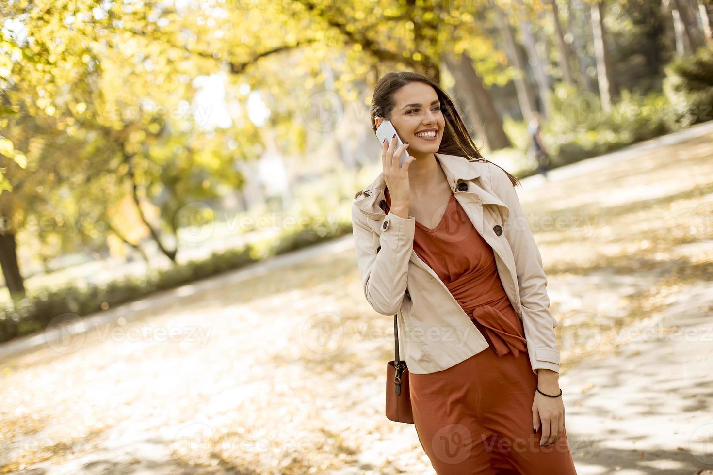 Happy young woman using cell phone in autumn park photo