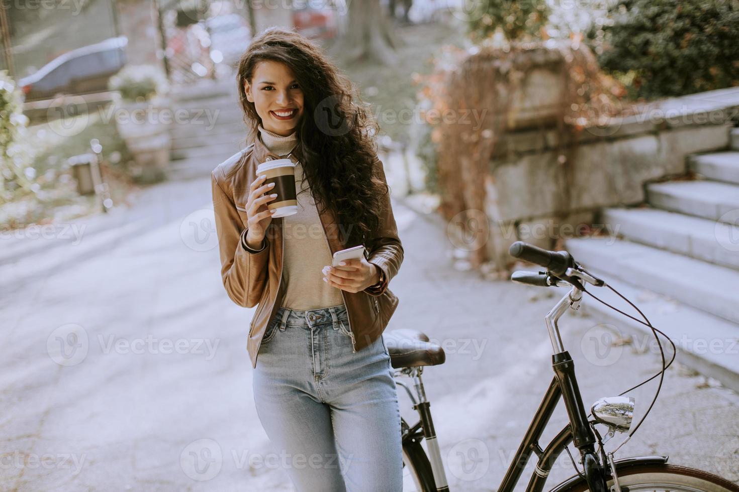 Young woman with mobile phone drink coffee to go by the bicycle on autumn day photo