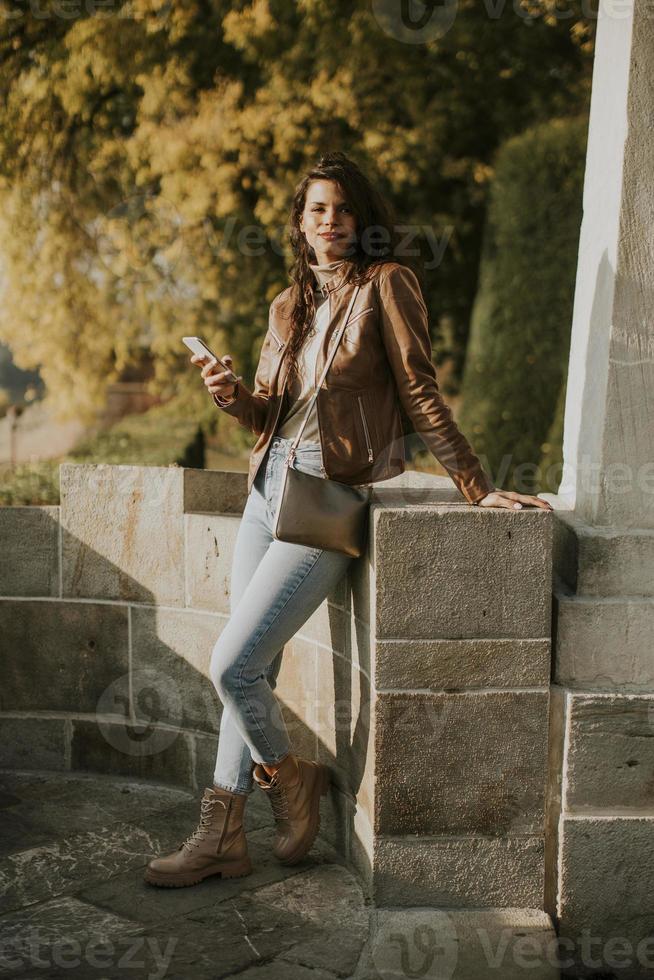 Young woman using mobile phone while standing in the autumn park photo