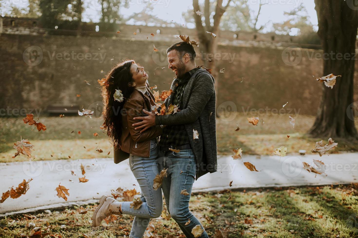 Pareja joven divirtiéndose con hojas en el parque de otoño foto