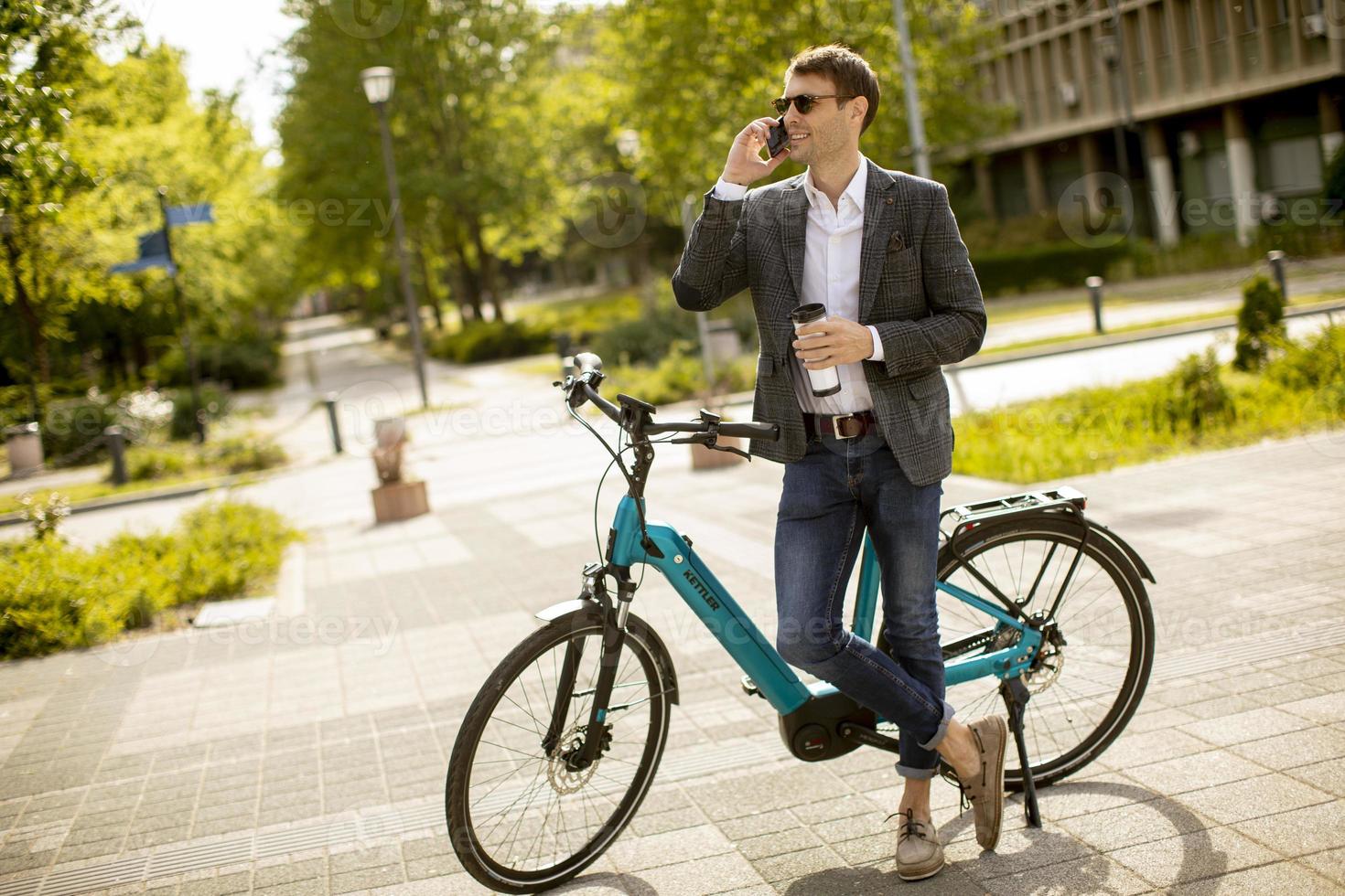 Young businessman using mobile phone by the ebike with takeaway coffee cup photo