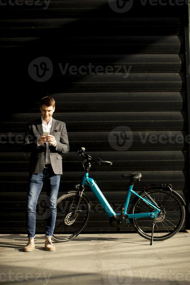 joven empresario de pie junto a la bicicleta eléctrica y usando un teléfono móvil foto