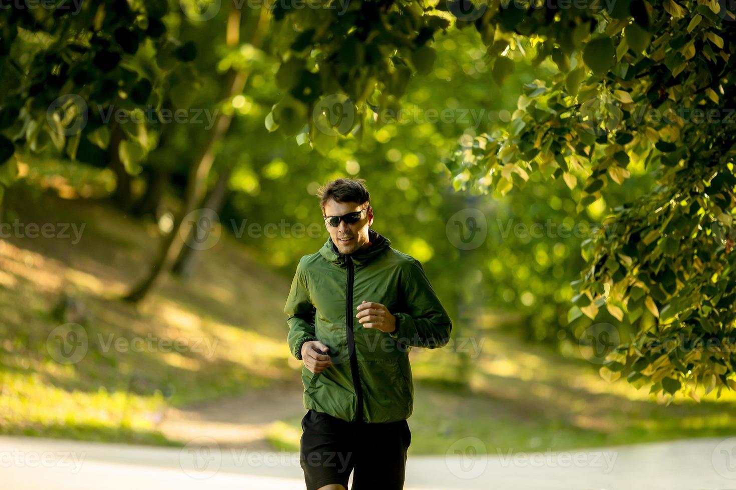 Athletic young man running while doing workout in sunny green park photo