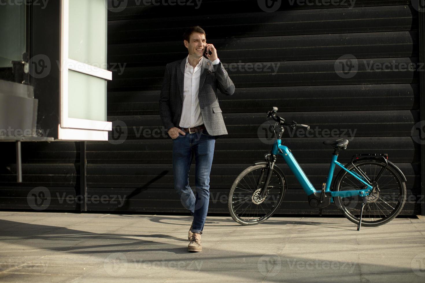 Young businessman walking away from the ebike and using mobile phone photo