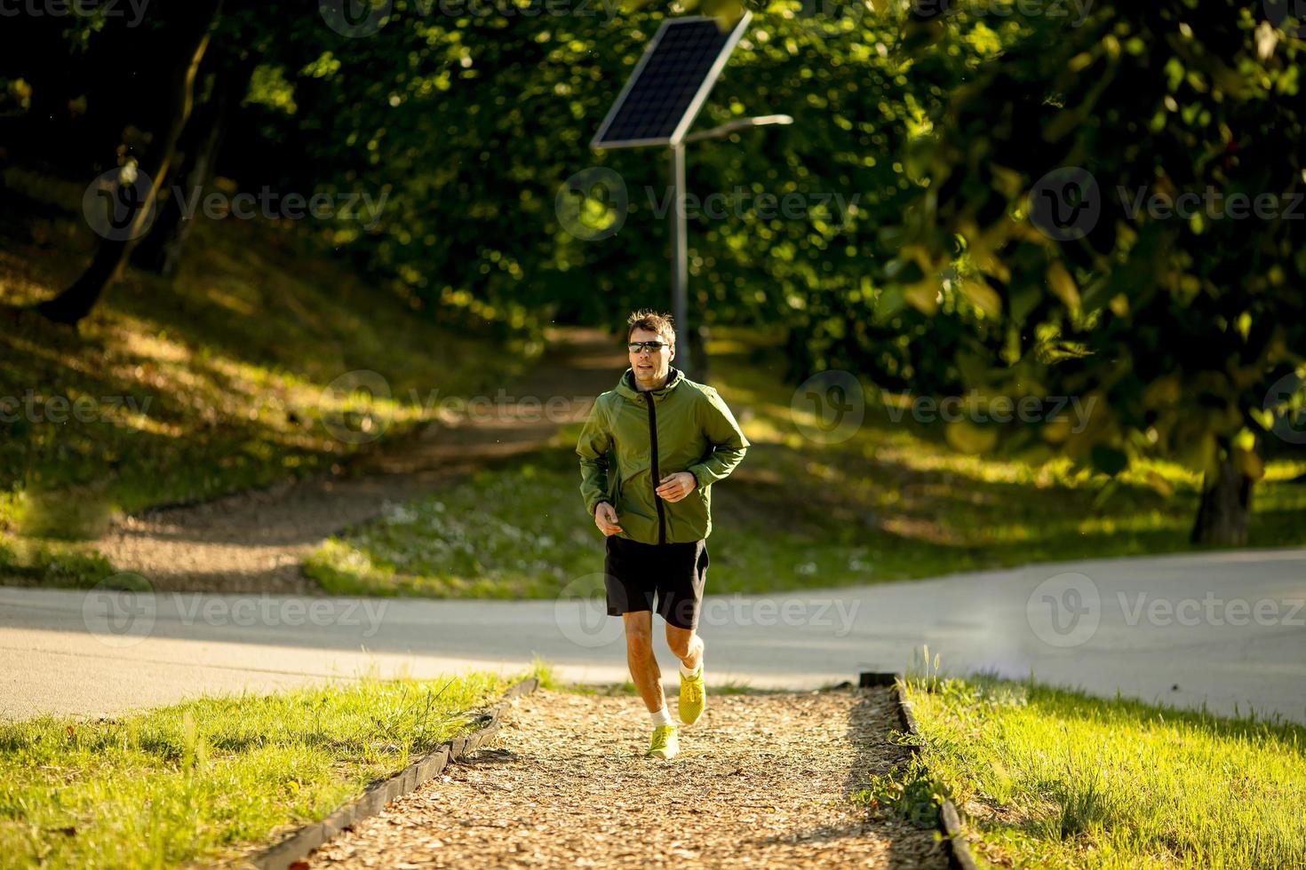 Atlético joven corriendo mientras hace ejercicio en el soleado parque verde foto