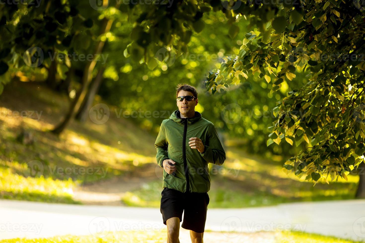Athletic young man running while doing workout in sunny green park photo