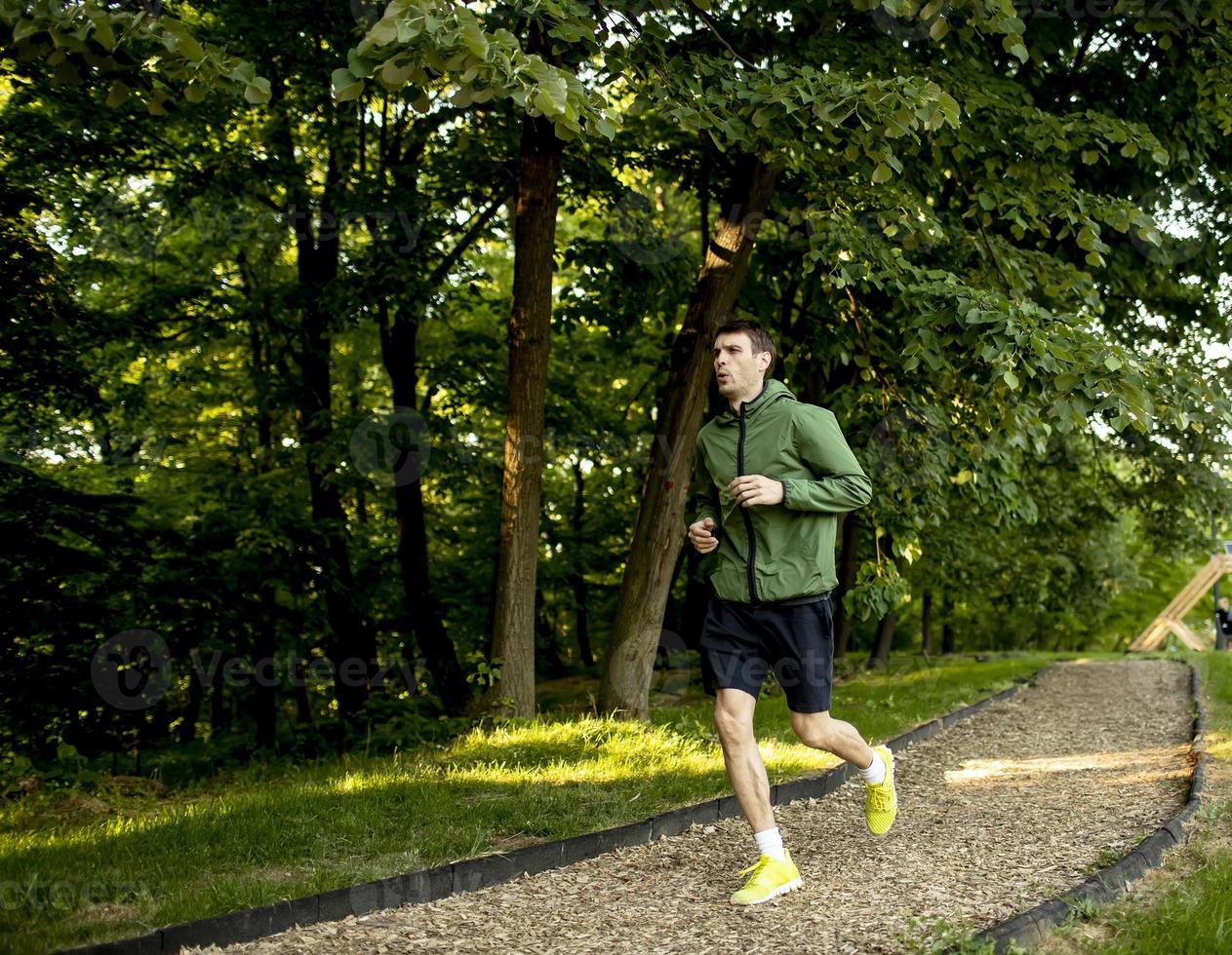 Athletic young man running while doing workout in sunny green park photo