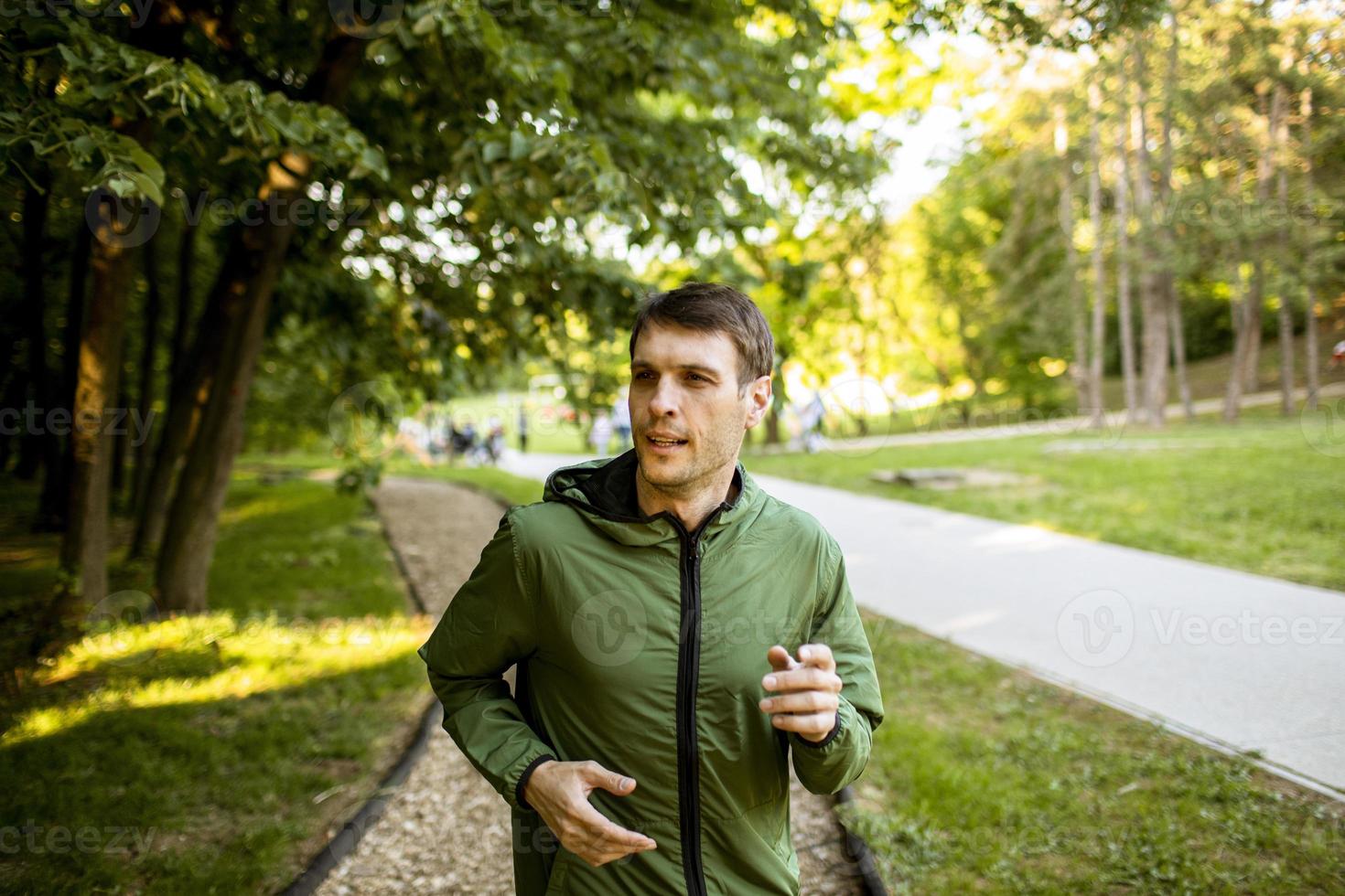 Athletic young man running while doing workout in sunny green park photo