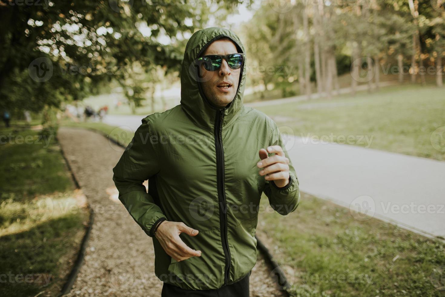 Athletic young man running while doing workout in sunny green park photo